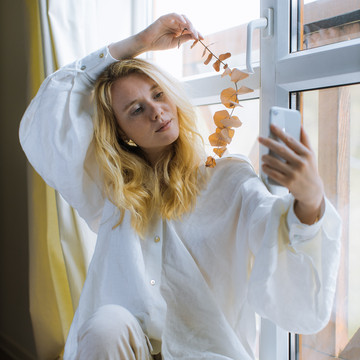 Chica frente a una ventana fotografiando con el móvil unas hojas